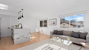 Una sala de estar moderna con una mesa de centro de vidrio, un sofá gris y una isla de cocina de mármol blanco.