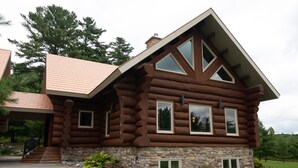 Une cabane en rondins avec des fondations en pierre, de grandes fenêtres et un toit en pente.