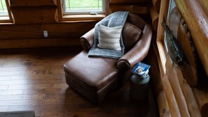 Une pièce chaleureuse dans un chalet en bois, avec un fauteuil en cuir, un plaid tricoté et un magazine posé sur le sol.