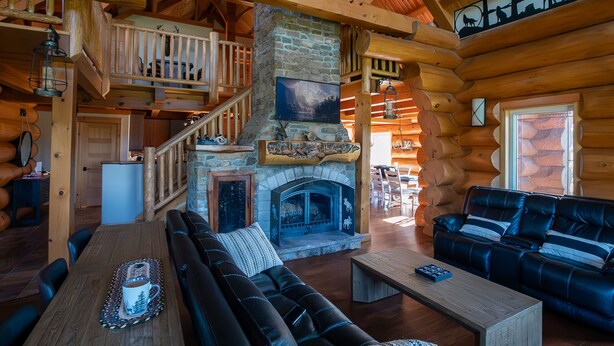 L’intérieur d’une cabane en rondins, avec une cheminée en pierre, un escalier en bois et un coin salon confortable.
