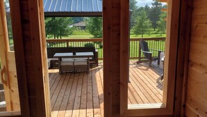 Une terrasse en bois avec une table et des chaises, un espace salon couvert et une vue sur un paysage verdoyant.