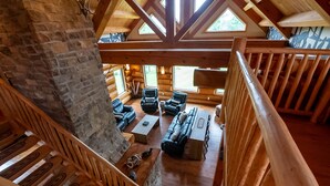 L’intérieur de cette vaste cabane en rondins est doté d’un plafond haut, de poutres en bois et d’un coin salon confortable avec des canapés et des fauteuils en cuir.