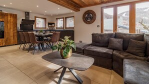 A modern kitchen with wooden accents, a dining area with a round table and chairs, and a living room with a sofa and a coffee table. - Chalet Lamartine - Valloire (VALLOIRE)