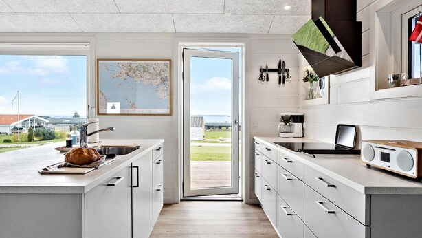 A modern kitchen with a large island, a coffee maker, and a view of a lake through the door.