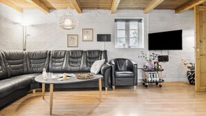 En moderne stue med en lædersofa i sektioner, en enkelt lænestol, et sofabord og et fjernsyn monteret på væggen.