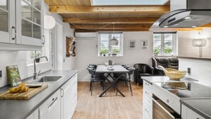 Et moderne køkken med hvide skabe, træloft og et spiseområde med sorte stole.