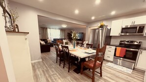A modern kitchen with stainless steel appliances, a dining area with wooden chairs, and a living room with a sofa and TV. - conveniently located home is perfect for families and friends , near Hershey ! (Palmyra)
