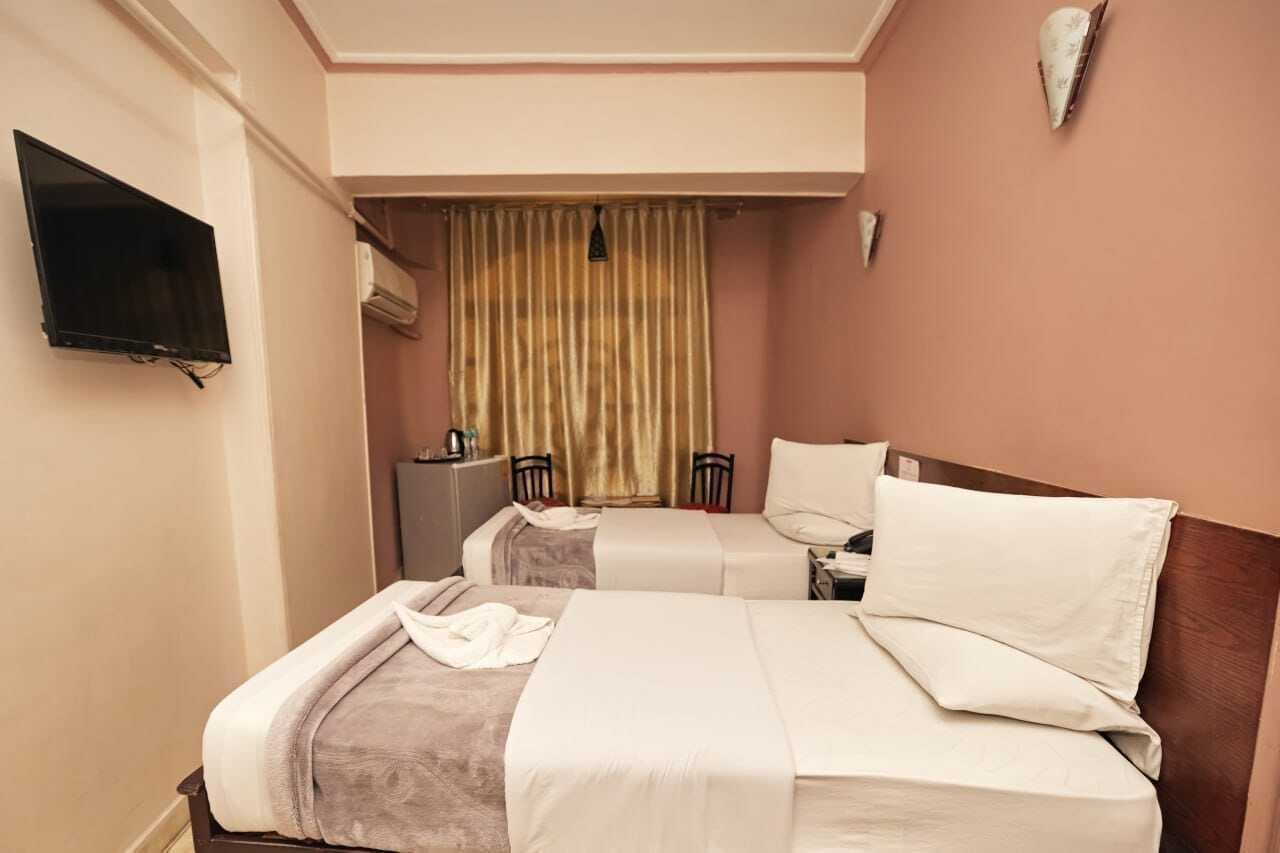 Habitació d'hotel amb dos llits, una televisió penjada a la paret i una finestra amb cortines.