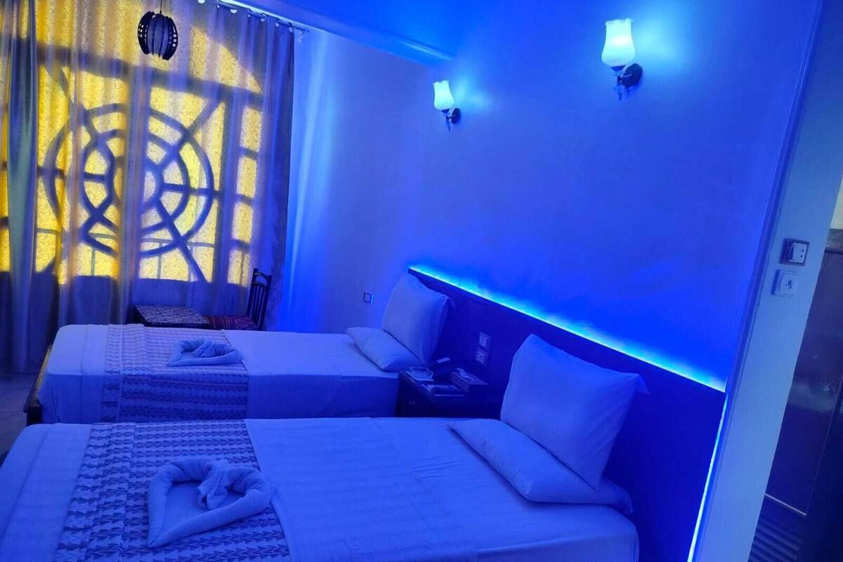 Habitación de hotel con dos camas, una mesita de noche y una lámpara de pared.