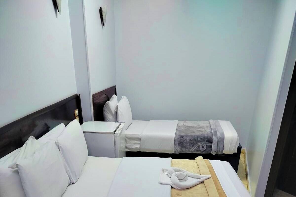 Habitación de hotel con dos camas, cada una con ropa blanca y una manta marrón.