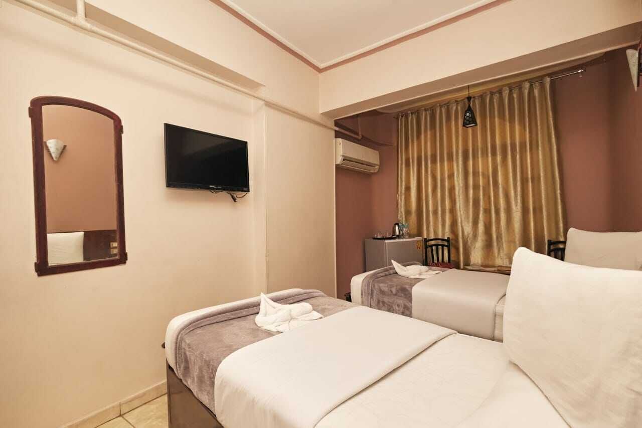 Een hotelkamer met twee bedden, een televisie, een airconditioning en een gordijn.