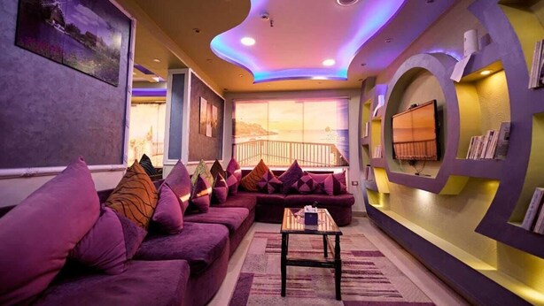 A modern living room with purple sofas, a coffee table, and a large window with a view.
