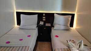 A hotel room with two single beds, each with a pillow and a small table. There are wall-mounted light fixtures above the beds.