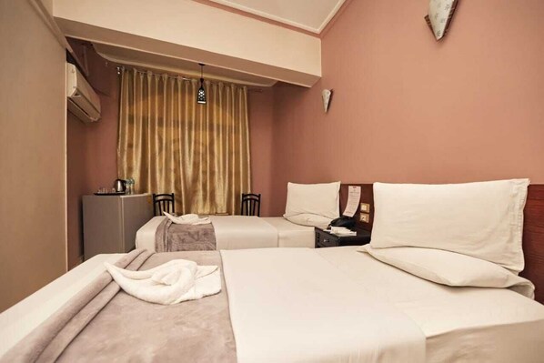 Una habitación de hotel con dos camas, un escritorio, una silla, un mueble pequeño y una cortina.