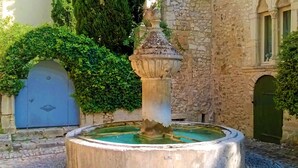 Una fuente de piedra con una columna central y una cuenca, rodeada de muros de piedra y follaje.