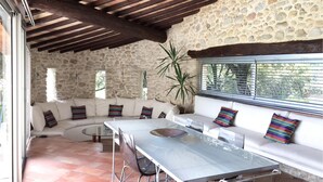 Un salón moderno con pared de piedra, techo de madera, mesa de comedor de cristal y sofá blanco con cojines de colores.