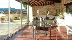 Un patio con una mesa y sillas de vidrio, un muro de piedra y vistas a las montañas.