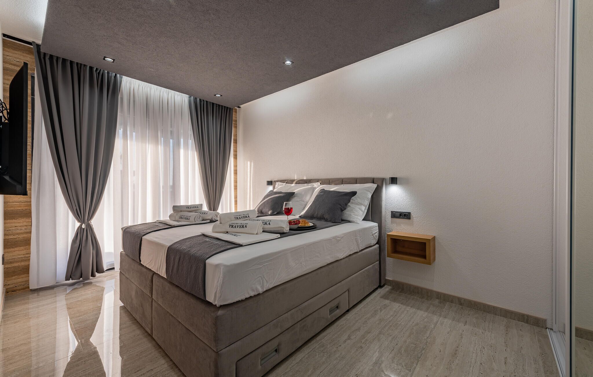 A modern bedroom with a large bed, bedside tables, and a TV mounted on the wall.