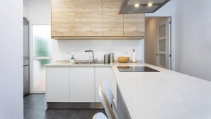 A modern kitchen with white cabinetry, a wooden accent wall, a stainless steel sink, and a black induction cooktop. - Home2Book Pleasant & Design Apt Santa Cruz Center (Santa Cruz de Tenerife)