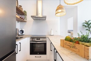 A modern kitchen with white cabinetry, a built-in oven, a stainless steel range hood, and a wooden fruit crate on the counter.