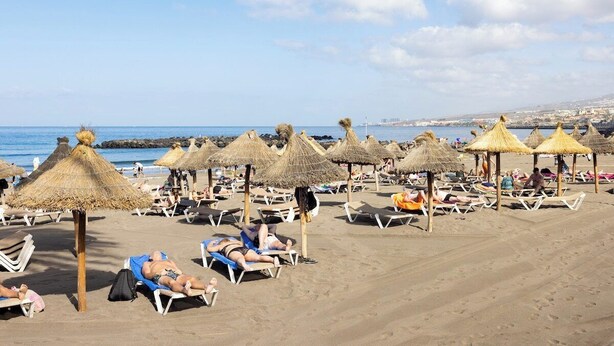 Une plage avec des chaises longues et des parasols en chaume.