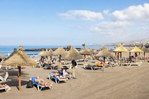 A beach with sun loungers and thatched umbrellas. - Home2Book Stylish Apt Terrace Las Américas (Playa de la Américas)