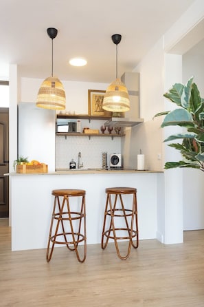 A modern kitchen with two hanging pendant lights, a built-in island with stools, and a large potted plant.