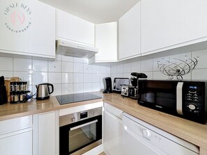 A modern kitchen with white cabinets, a stainless steel kettle, a coffee maker, a microwave, and a dishwasher. - Entre Ciel et Mer - Vue Mer - 3 CH & Parking (Bray-Dunes)