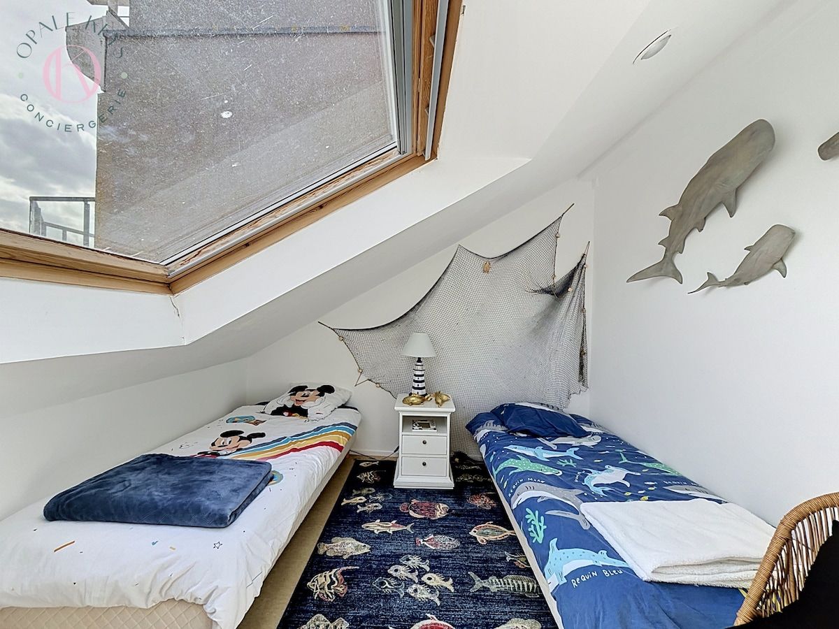 Una habitación pequeña y funcional con dos camas individuales, una mesita y una ventana.