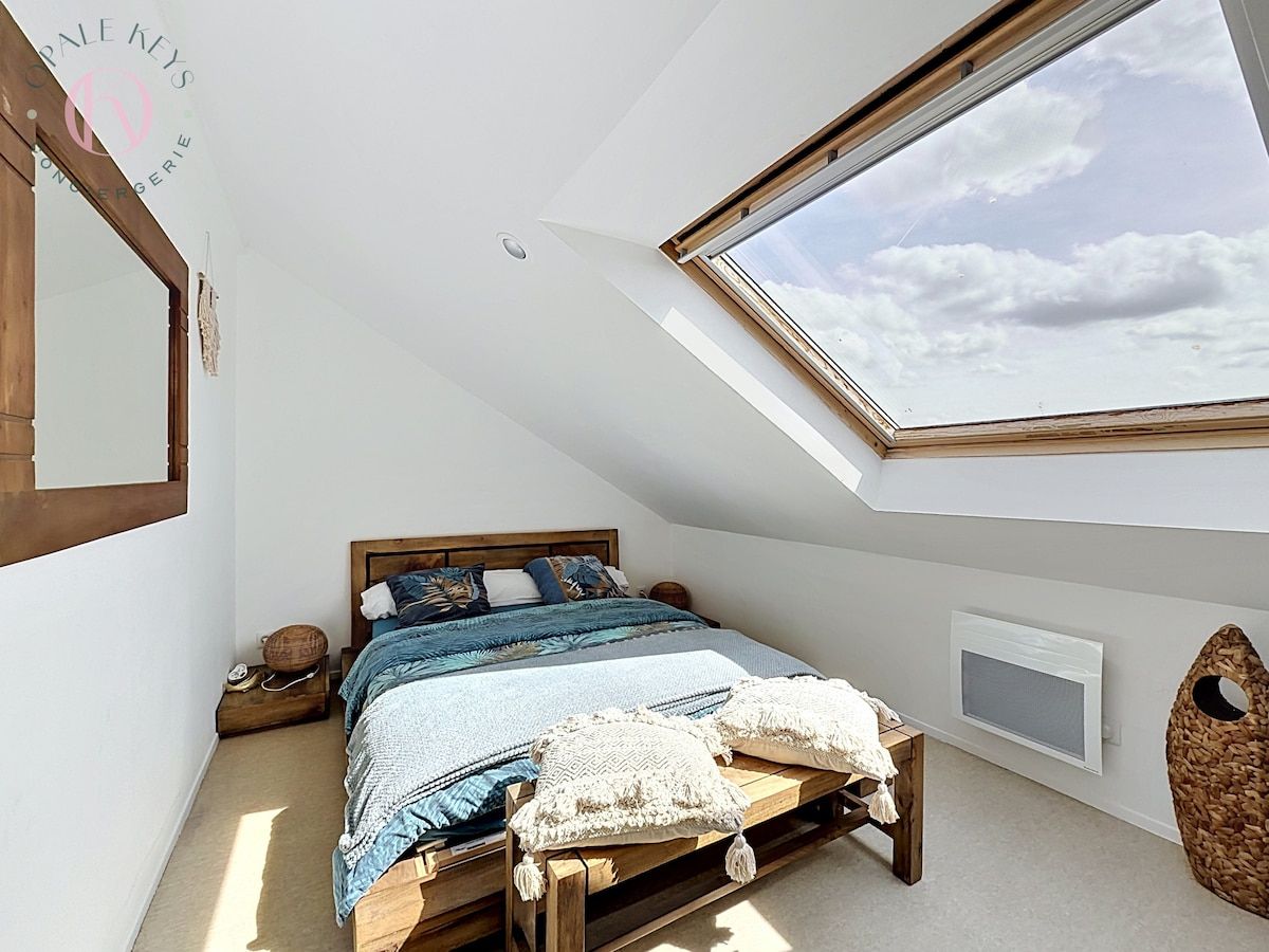 Une chambre avec un plafond en pente, un puits de lumière, un lit avec un cadre en bois et un téléviseur fixé au mur.