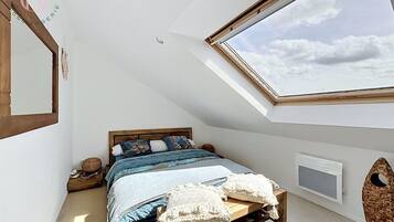 Une chambre avec un plafond en pente, un puits de lumière, un lit avec un cadre en bois et un téléviseur fixé au mur.