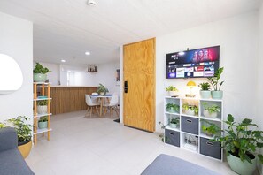 A modern reception area with a wooden door, a reception desk, a TV displaying a streaming service, and potted plants.