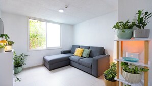 A modern living room with a grey sectional sofa, a white TV stand, and a variety of potted plants. - Apartment with parking in Tlaquepaque Pueblo Mágico (Guadalajara)