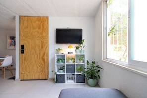 Une pièce avec une porte en bois, un téléviseur fixé au mur, une étagère pour les plantes et une fenêtre donnant sur un beau paysage.