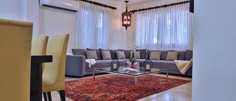 A modern living room with a grey sofa, yellow chairs, a glass coffee table, and a red patterned rug.