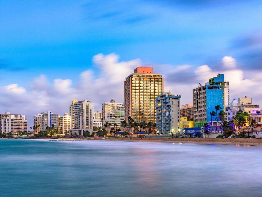 A coastal cityscape with high-rise buildings, a beach, and palm trees.