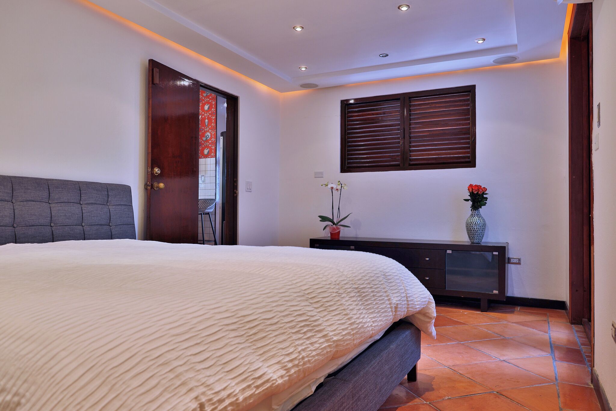 Un dormitorio con cama, cómoda, ventana con persianas y puerta.