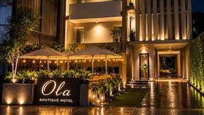 Un hotel moderno con varios balcones, mobiliario exterior y una entrada bien iluminada.