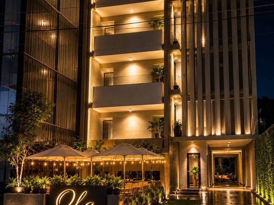 Un hotel moderno con varios balcones, mobiliario exterior y una entrada bien iluminada.