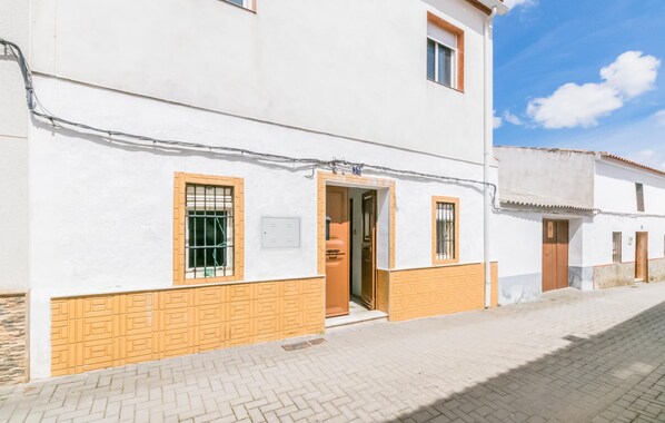 A white building with a wooden door and window frames, a visible electrical box, and a paved street. - 3 bedroom awesome home in Villanueva del Rey (Villanueva del Rey)