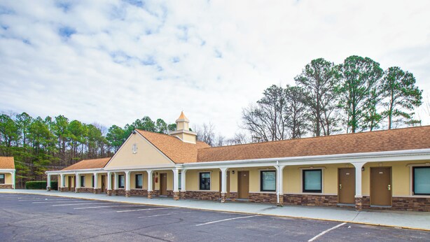 A motel with a row of rooms, a parking lot, and a large tree in the background. - WHITEHOUSE MOTEL (Richmond)