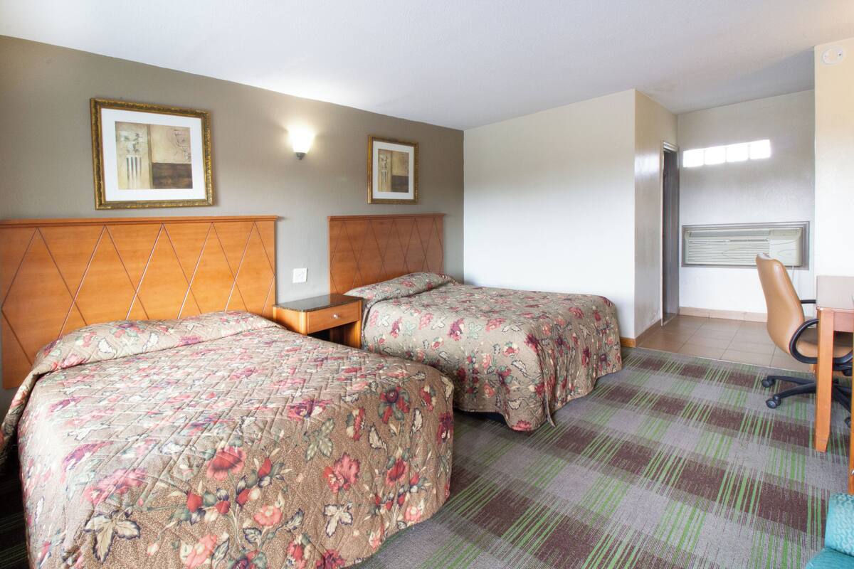 A hotel room with two beds, a desk, and a chair.