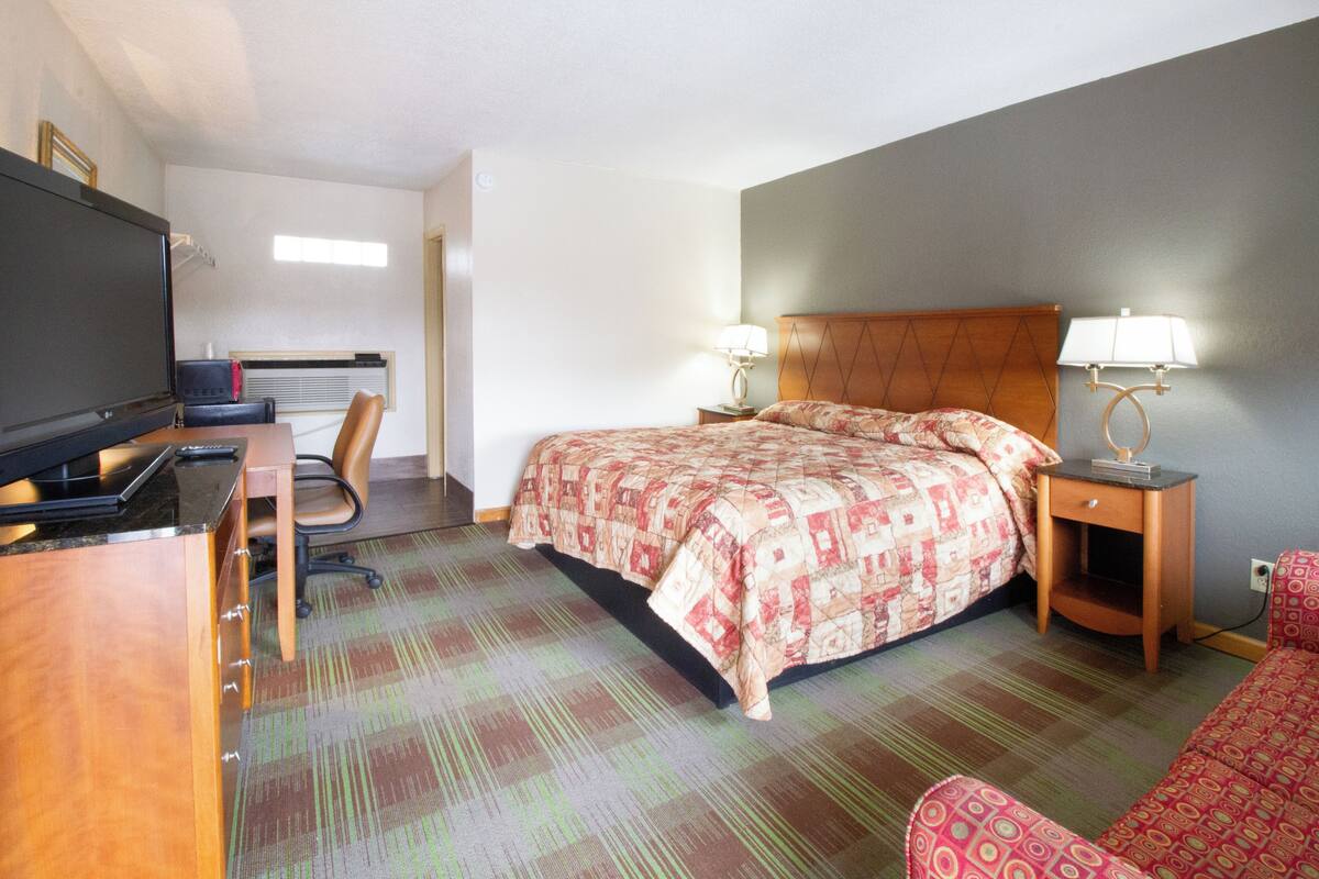 A hotel room with a bed, a desk with a computer, a chair, and a TV.