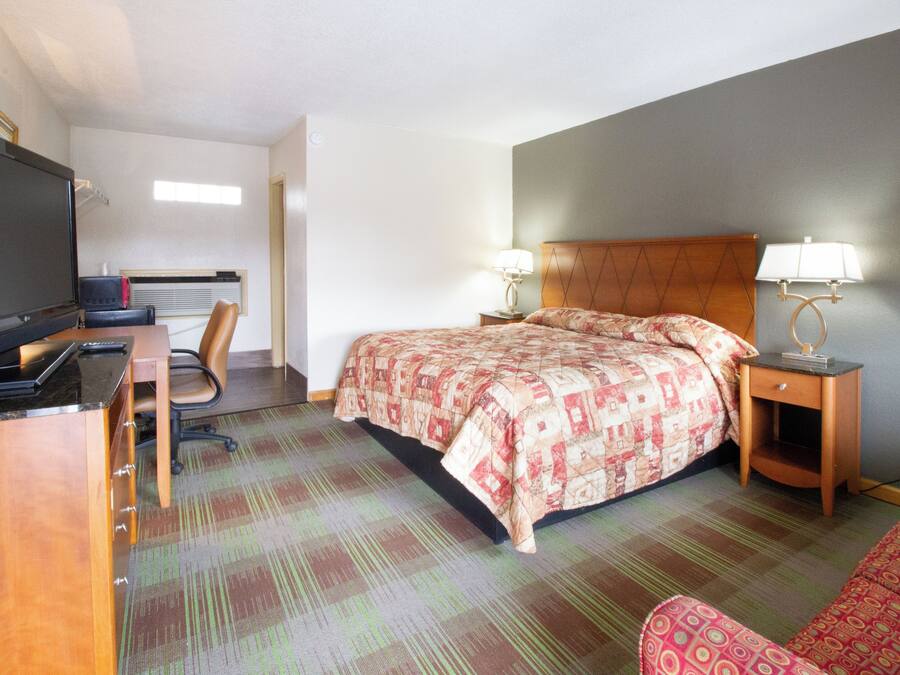 Una habitación de hotel con una cama, un escritorio con una computadora, una silla y un televisor.