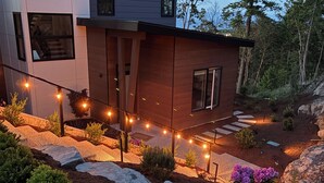 A modern house with a wooden exterior, a stone pathway, and string lights.