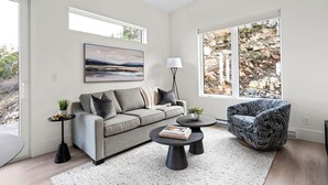 A modern living room with a grey sofa, a black coffee table, a patterned armchair, and a large window with a rocky landscape view.