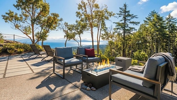 An outdoor seating area with chairs and a fire pit, surrounded by trees and overlooking a scenic view.