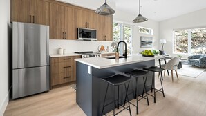 A modern kitchen with wooden cabinets, stainless steel appliances, and a central island with bar stools. - Mountain Suite | Ocean View Fire Pit | Full Kitch (Lantzville)