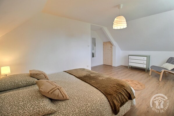 A bedroom with a large bed, a dresser, a chair, and a hanging light fixture.