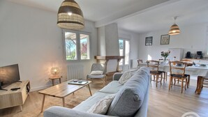 A modern living room with a sofa, coffee table, and dining area with chairs and a table. - Le Rocher - Trelivan (TRELIVAN)